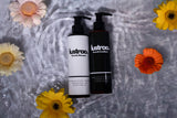 Two bottles of 'lustraa' shampoo and conditioner on a textured surface with flowers around.