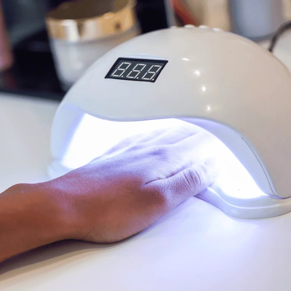 Hand under a nail drying lamp with a digital timer on a white surface