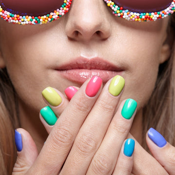 Close-up of a person with colorful nail polish wearing sunglasses with a candy-like frame.